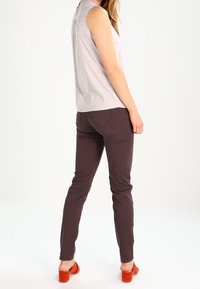 Canotta grigia chiara senza maniche abbinata a pantaloni aderenti viola scuro, con una superficie liscia. Sandali con tacco arancioni completano il look.