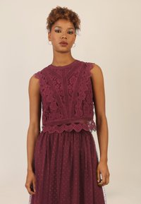 Burgunderfarbener Spitzentop mit gewellten Kanten und Blumenmustern, kombiniert mit einem transparenten, gepunkteten Rock, der ein geschichtetes Designmerkmal aufweist.