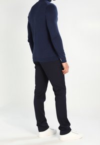 Marinblå ribbad tröja med hög halskrage som kombineras med mörka byxor och vita sneakers, vilket visar en figurnära silhuett och slät textur.