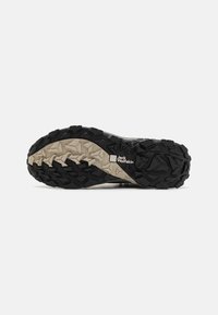 Suola nera e beige di una scarpa con un motivo di battistrada texturizzato e multidirezionale e un logo vicino al tallone.