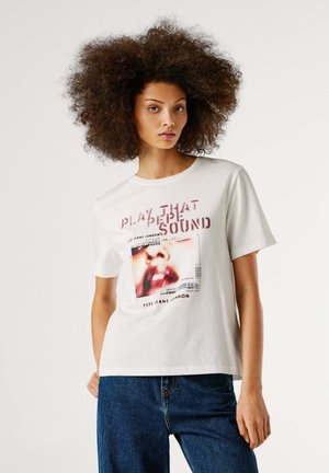 Camiseta blanca de algodón con gráfico impreso de un rostro y texto "PLAY THAT DEEP SOUND", mangas cortas y corte holgado, combinada con pantalones de mezclilla azul.