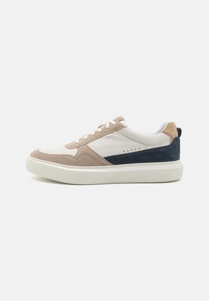 Adidași din suede și piele cu o schemă de culori albă, bej și albastru închis. Prezintă o talpă texturată și accente contrastante. Design cu șireturi.