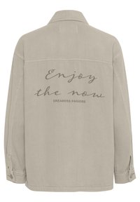 Beige denim jack met een achterkant ontwerp met de teksten "Enjoy the now" en "DREAMERS PARADISE" in cursief. Klassieke kraag en knoopmanchetten.