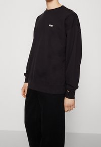 Felpa nera con collo a giro, con logo "Levi's" in bianco, vestibilità ampia, polsini e orlo a costine, abbinata a pantaloni neri.