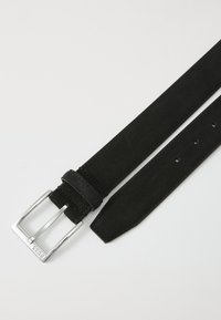 Curea din suede negru cu o cataramă rectangulară argintie. Prezintă o textură netedă și mai multe găuri de ajustare de-a lungul curelei.