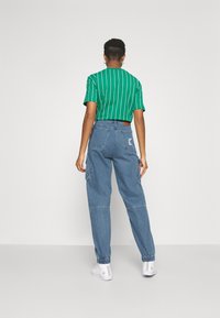 Grönrandig t-shirt med korta ärmar, ihopparad med lösa blå jeansbyxor med elastiska muddar och bakfickor. Vita sneakers fulländar outfiten.