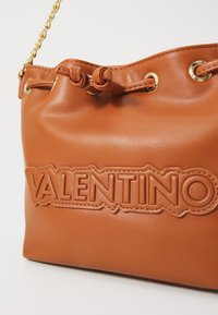 Borsa in pelle tan con accessori dorati, dotata di chiusura a cordoncino e logo "VALENTINO" impresso sul davanti. Texture liscia.