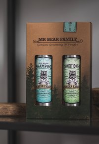 Set regalo contenente due lattine cilindriche: shampoo azzurro chiaro e balsamo verde, entrambi con grafiche di orsetti, in una scatola marrone strutturata.