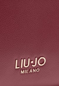 Bolso de cuero burdeos con superficie texturizada, con un logo dorado en relieve que dice "LIU•JO MILANO" en el centro inferior.