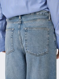 Ljusblå denimjeans med avslappnad passform, med två bakfickor, synliga sömmar och midjeres midjeband.