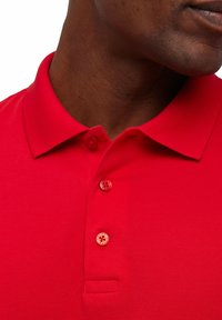 Polo shirt rosso con colletto classico, tre bottoni e tessuto texture. I bottoni presentano un design a contrasto con motivi visibili.