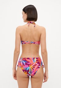 Set di bikini con un vivace motivo tropicale di foglie in rosa, blu e giallo su uno sfondo viola scuro. Legature al collo e ai lati.