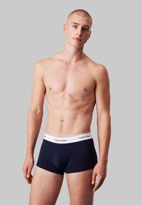 Boxeri pentru bărbați de culoare bleumarin, cu un elastic alb pe talie inscripționat cu logo-ul "Calvin Klein", confecționați dintr-un material neted, cu un design ajustat.