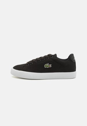 Black canvas sneakers with white rubber sole, featuring black eyelets and a green crocodile logo on the side. Classic low-top design.