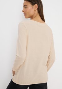 Long-sleeve beige top with horizontal stripes, round neckline, and soft fabric. Features a relaxed fit and subtle side slits.