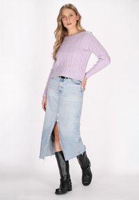 Maglione a treccia viola, gonna midi in denim chiaro con spacco frontale e stivaletti neri alla caviglia. Dettagli osservati includono polsini a coste e orlo grezzo.
