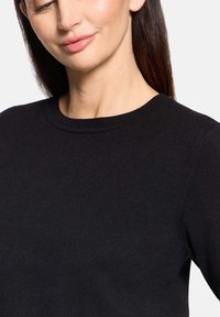 Pull noir en maille avec un col rond et un ourlet côtelé. Texture lisse et silhouette ajustée, mettant en valeur le savoir-faire du vêtement.