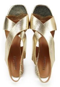 Gouden metallic hoge hakken sandalen met kruislings straps en een gestructureerde afwerking. Voorzien van een vierkante neus en subtiele glitteraccenten op de hak.