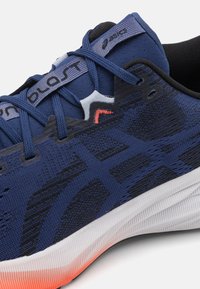 Baskets de sport bleues avec une tige en tricot texturé, des accents noirs contrastants, une semelle intermédiaire blanche et des détails orange sur la semelle extérieure.