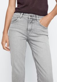 Jean en denim gris avec un design ajusté. Les caractéristiques incluent une poche avant, des coutures visibles et une surface légèrement texturée.