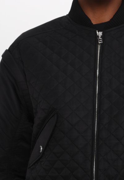 Giubbotto bomber trapuntato nero con colletto a coste, zip argentata e tasca laterale inclinata. Texture liscia e vestibilità sagomata.