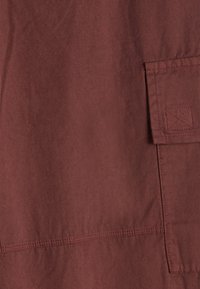 Tessuto bordeaux con una consistenza morbida; presenta una tasca a patch con cuciture visibili e una linea di cucitura dritta al centro.