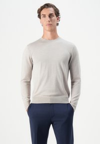 Suéter de manga larga gris claro, hecho de una tela suave. Cuello redondo, forma ajustada, puños y cinturilla de canalé. Combinado con pantalones azul marino.