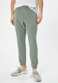 Lichte, olijfgroene joggerbroeken met een elastische taille, taps toelopende enkels en zijzakken; gemaakt van een gladde, rekbare stof.