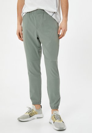 Leichte, olivgrüne Jogginghosen mit elastischem Bund, schmal zulaufenden Knöcheln und Seitentaschen; aus einem glatten, dehnbarem Material gefertigt.