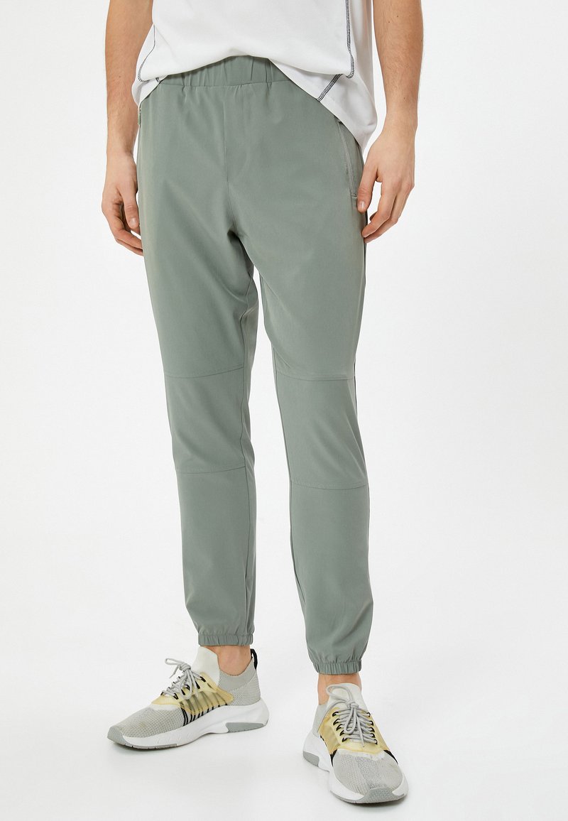 Lichte, olijfgroene joggerbroeken met een elastische taille, taps toelopende enkels en zijzakken; gemaakt van een gladde, rekbare stof.