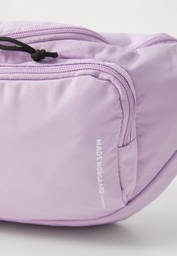 Borsa lilla chiaro con texture liscia, dotata di una cerniera prominente e del nome del marchio "MADS NØRGAARD" in bianco. Design compatto e moderno.