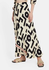 Falda maxi en tejido crema con patrones abstractos en negro y un acento horizontal rojo. El diseño tiene una silueta fluida.