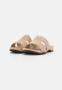 Beige suède instapsandalen met een open teen, twee uitsneden aan de zijkanten en een platte zool met een getextureerde zwarte rubberen buitenzool.