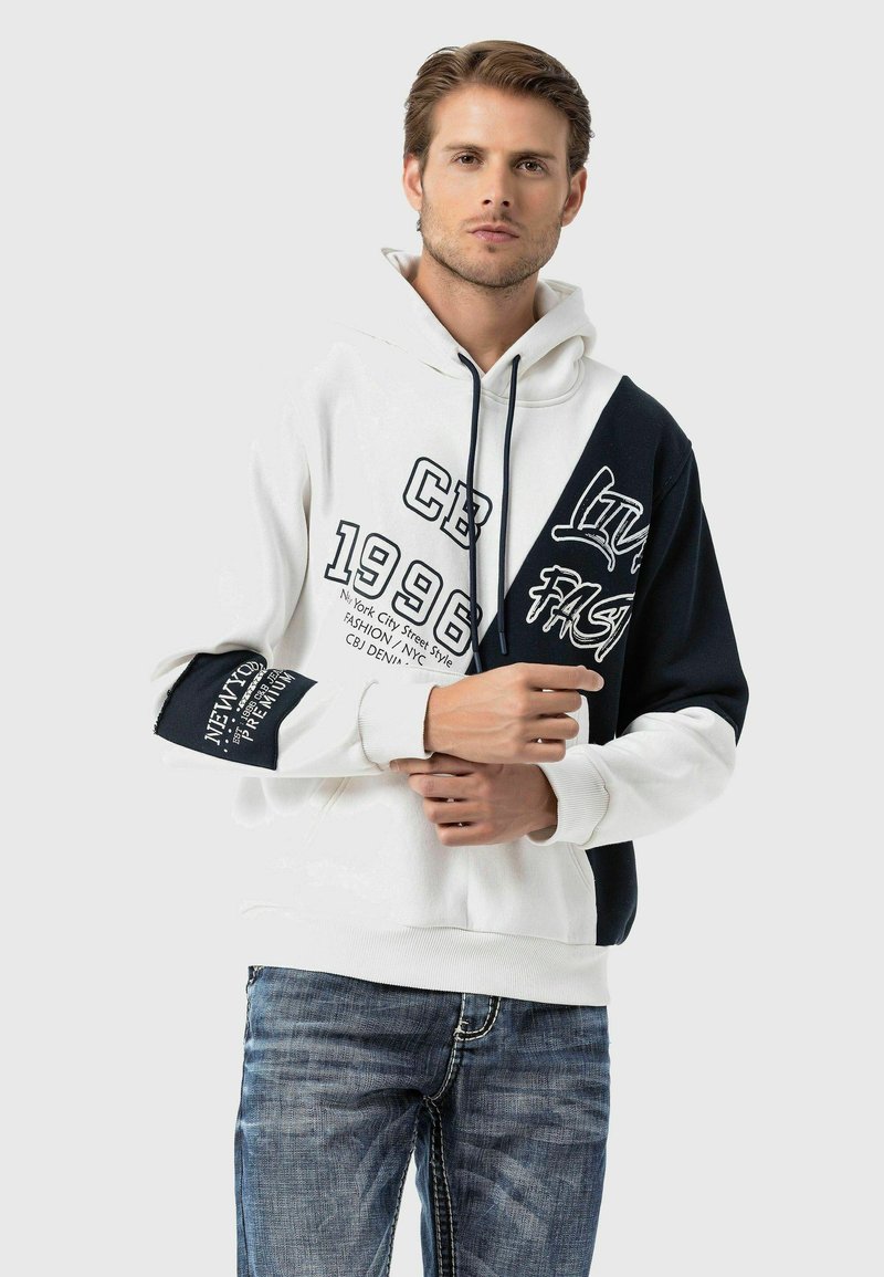 Kapuzensweatshirt in Weiß und Schwarz mit grafischem Text, verfügt über ein mehrfarbiges Design, weichen Stoff und einen lässigen Schnitt. Darunter sind Jeans abgebildet.