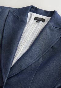 Navy blazer made of textured fabric, featuring a notched collar, and an interior striped lining. Brand label visible inside.
