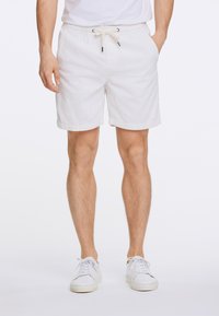 Pantalones cortos de pana blanca con cintura elástica y cordón. Presentan bolsillos laterales y un dobladillo en las piernas. Combinados con zapatillas blancas.