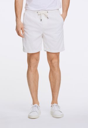 Pantalones cortos de pana blanca con cintura elástica y cordón. Presentan bolsillos laterales y un dobladillo en las piernas. Combinados con zapatillas blancas.