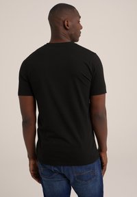 Tricou negru din bumbac, cu mâneci scurte, guler rotund și o croială lejeră. Purtați cu blugi albaștri, evidențiind o textură netedă și un design simplu.