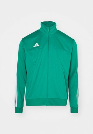 Vihreä vetoketjullinen takki, joka on valmistettu pehmeästä materiaalista. Takissa on korkea kaulus, valkoiset kolme raitaa hihoissa ja kolmio design etupuolella.