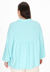 Himmelblaues, geripptes Shirt mit Kragen, Peplum-Design und langen Ärmeln. Es hat eine lockere Passform mit strukturiertem Stoff und subtiler Glanz.