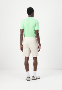 Short-sleeve mint green polo shirt paired with light beige shorts. Model wears white socks and black-and-white sneakers.plain background.