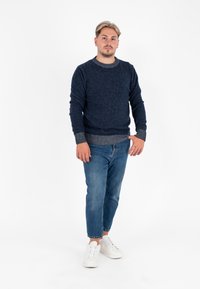 Maglione blu navy lavorato a maglia con finitura testurizzata, con colletto rotondo e polsini a coste, abbinato a jeans azzurri chiari e sneakers bianche.