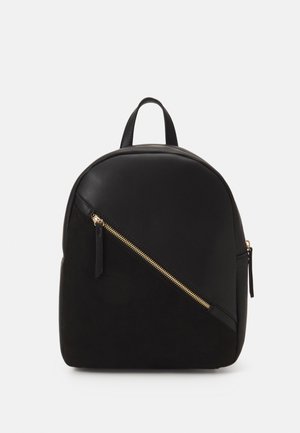 Mochila negra con bolsillo frontal con cremallera dorada diagonal, asa superior de cuero y forma redondeada sobre fondo blanco.