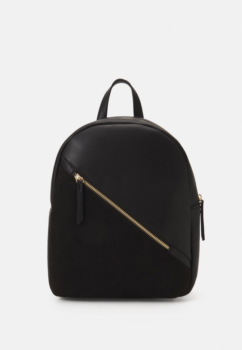 Sac à dos noir avec poche zippée diagonale en or à l'avant, poignée supérieure en cuir et forme arrondie sur fond blanc.