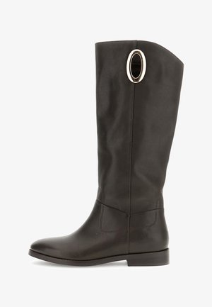 Bota de cuero marrón oscuro alta con suela plana y detalle en forma de óvalo dorado cerca de la parte superior en el lado exterior.