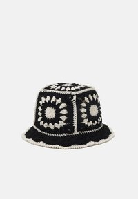 Chapeau seau au crochet en noir et blanc avec des motifs circulaires. Forme structurée avec un large bord et une finition texturée.