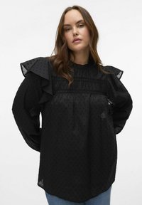 Blusa nera con maniche arricciate, tessuto testurizzato con motivi a pois e dettagli arricciati sul petto, dalla vestibilità ampia e scollatura rotonda.