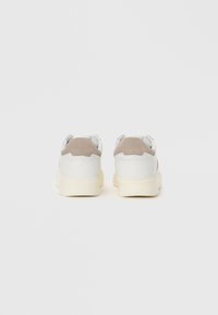 Sneaker bianche con una superficie in pelle liscia e accenti in suede beige. Forma arrotondata con una suola spessa di colore crema, caratterizzata da dettagli di cucitura minimi.