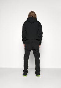 Svart hoodie med en lös passform, parat med svarta smalrandiga byxor och färgglada sneakers. Slät textur med minimal detaljering.