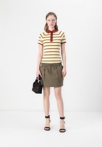 Stripet polo skjorte i gul og burgunder, paret med en khaki mini-skjørt med frontlommer. Svarte stroppede hæler og en liten mørk veske.